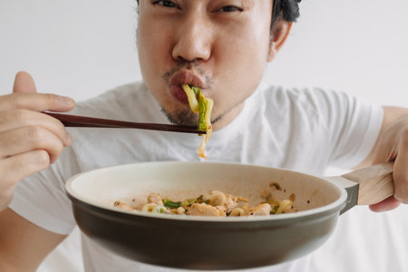 Close up of funny asian man eating his homemade lunch straight on the pan.の写真素材