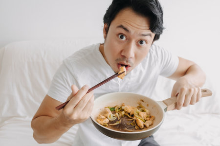 Close up of funny asian man eating his homemade lunch straight on the pan.の写真素材