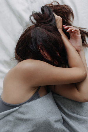 Woman does not want to wake up, using her arms to block the morning light.の写真素材
