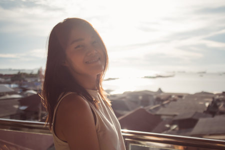 Close-up head shot portrait of happy asian woman enjoy the sunset and sea view.の写真素材