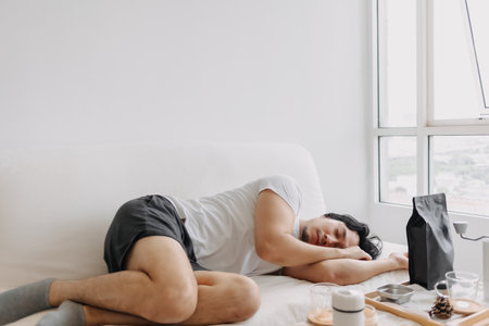 Asian man is taking a nap on the sofa after finish making the coffee.の写真素材