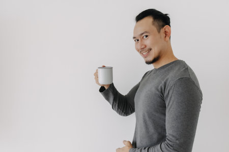 Happy smile face Asian man in grey fleece base layer drinking hot drink on white.の写真素材