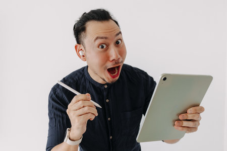 Surprised creative freelance Asian man with earbuds work tablet isolate white.の写真素材