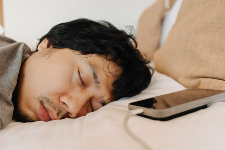 Close up face of sleepy asian man slept with his mobile phone left near his headの写真素材