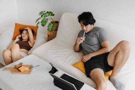 Asian couple lover, man working at home while woman is having a phone call.の写真素材