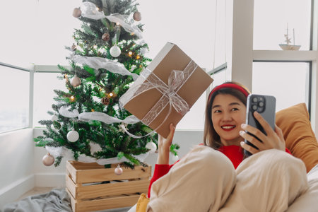Happy red shirt Asian woman making a video call for holiday greeting with her friends and family showing the Christmas tree. . High quality photoの写真素材