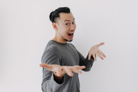 Wow surprise face Asian man in grey fleece base layer offer present on white.の写真素材