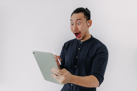 Surprised creative freelance Asian man with earbuds work tablet isolate white.の写真素材