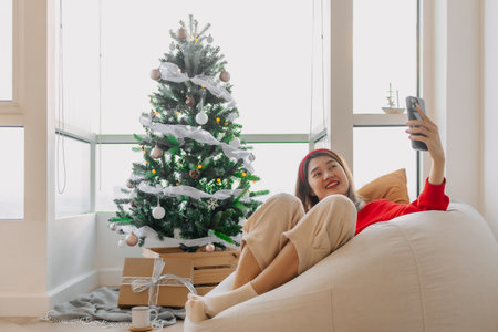Happy red shirt Asian woman making a video call for holiday greeting with her friends and family showing the Christmas tree. . High quality photoの写真素材