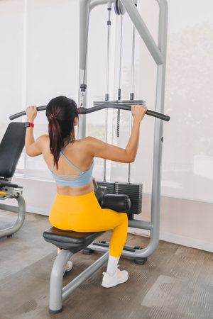 Asian woman in yellow blue fitness outfits do Cable Lat Pull Down back muscles.の写真素材