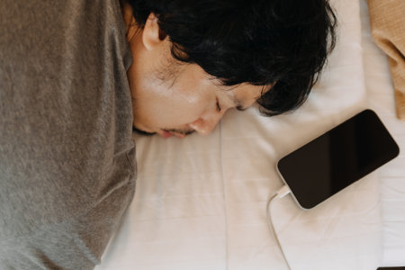 Close up face of sleepy asian man slept with his mobile phone left near his headの写真素材