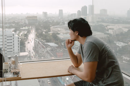 Lonely single asian man looking out to through the windows of apartment.の写真素材