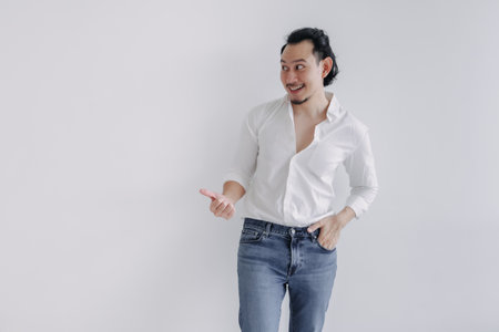Smile long hair Asian man bun in white shirt and jean pointing at empty space.の写真素材