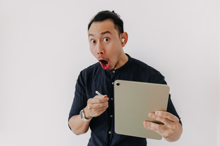 Surprised creative freelance Asian man with earbuds work tablet isolate white.の写真素材