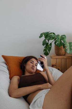 Happy asian woman using mobile phone relaxed on sofa in the living room.の写真素材