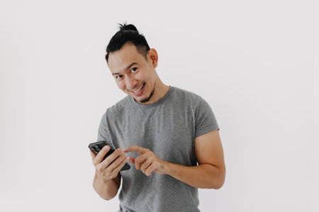 Happy smile face of Asian man in grey t-shirt using smartphone app on white.の写真素材