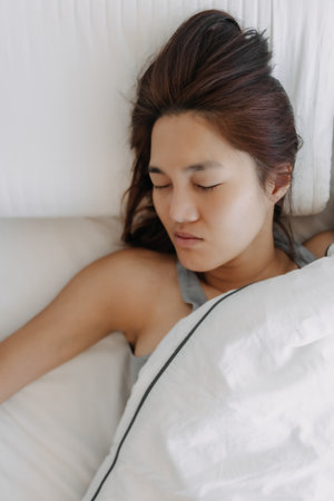 Asian woman sleeping on white bed, wake up late.の写真素材