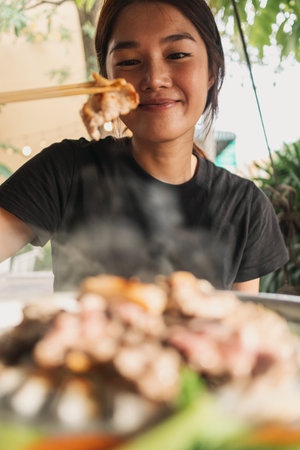 Close up of Asian woman eating Moo Kra Ta or Thai BBQ buffet.の写真素材