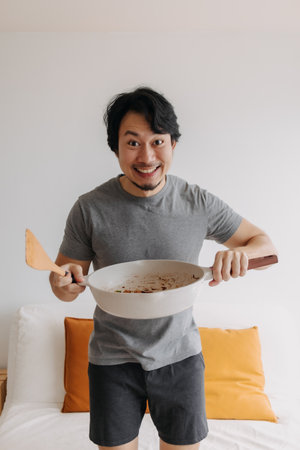Vertical photo of happy asian man presents and offering his meal in the pan.