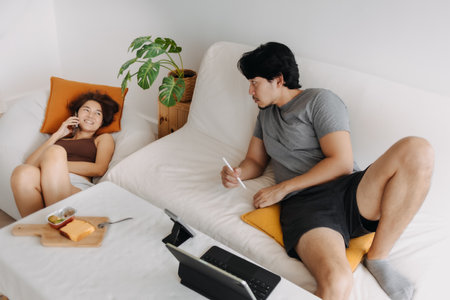 Asian couple lover, man working at home while woman is having a phone call.の写真素材