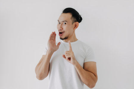 Funny tricky face Asian man telling secret in white t-shirt isolate on white.の写真素材
