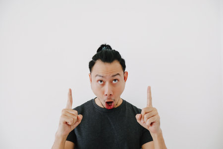 Wow and impressive Asian man hand pointing in black t-shirt isolate on white.