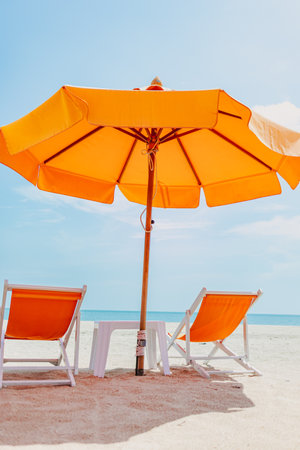 Vivid orange umbrella and chair set on the beach with blue sunny sky.の写真素材