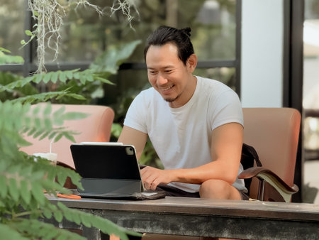 Happy freelance Asian man working online on his tablet computer in the cafe.の写真素材