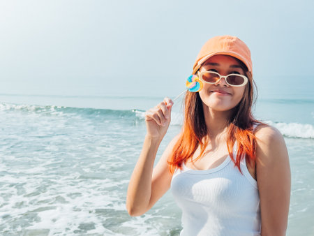 Young asian woman with colorful lollipop and orange hat enjoy the beach in Thailand.の写真素材