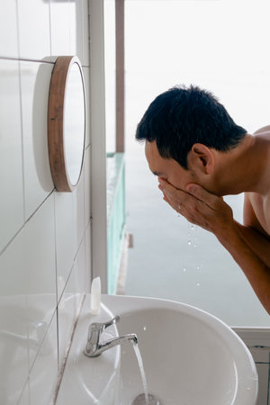 Asian man washing his face in front the mirror in the bathroom in the morning with view.