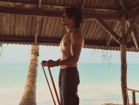 Man exercise and workout with rubber band in the hut by the sea. Beach relaxed vibe in Asia.の写真素材