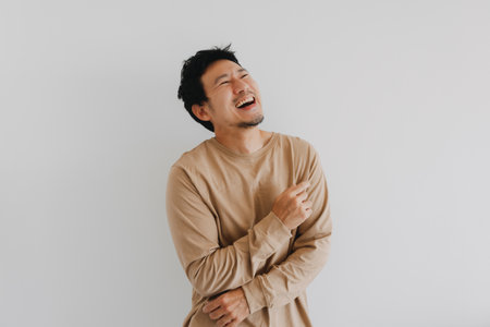 Young Asian male enjoys a hearty laugh while standing against white backgroundの写真素材
