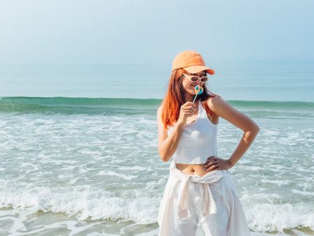 Young asian woman with colorful lollipop and orange hat enjoy the beach in Thailand.の写真素材