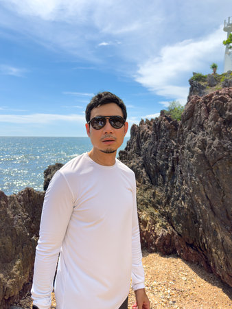 Man standing beside rocks with ocean and cloudy sky in the backgroundの写真素材