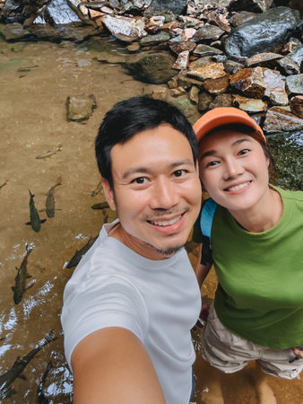 Man and woman standing in shallow stream surrounded by rocks and natureの写真素材