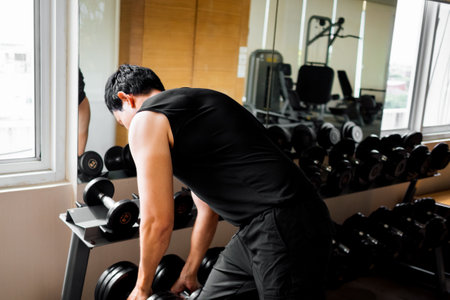 Focused male athlete preparing for weight training by selecting dumbbellの写真素材