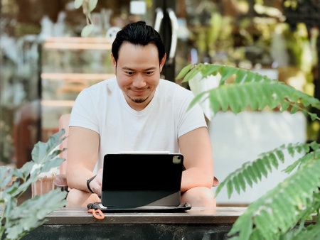 Happy freelance Asian man working online on his tablet computer in the cafe.の写真素材