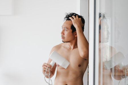 Asian male grooming beside glass mirror in bright clean modern bedroomの写真素材