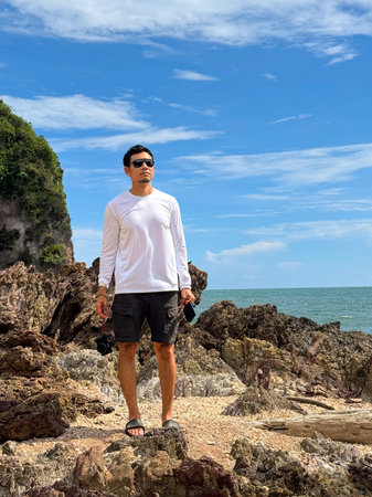 Traveler enjoying the scenic view at tropical rocky beach under bright daylightの写真素材