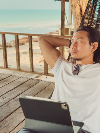Man working online with computer on the hammock by the beach, Digital nomad vibe.の写真素材