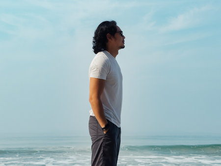 Asian man wears white t-shirt and sunglasses enjoy walking on the beach in Thailand.の写真素材