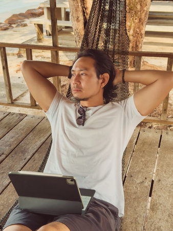 Man working online with computer on the hammock by the beach, Digital nomad vibe.の写真素材