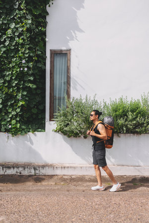Asian man tourist backpacker walking on the street passing white hotel building.の写真素材