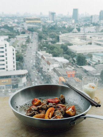 Pan of stir-fried seafood and vegetables by window overlooking urban skylineの写真素材