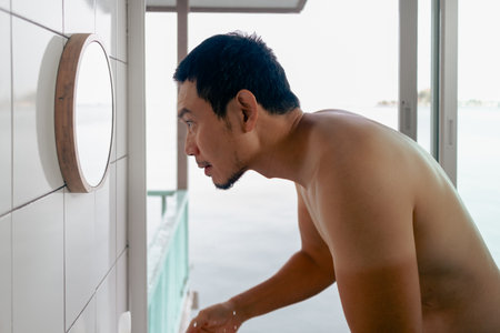 Asian man washing his face in front the mirror in the bathroom in the morning with view.の写真素材