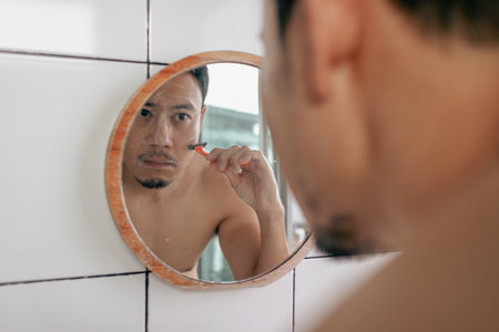 View from behind the shoulder of asian man shaving his beard in the bathroom.の写真素材