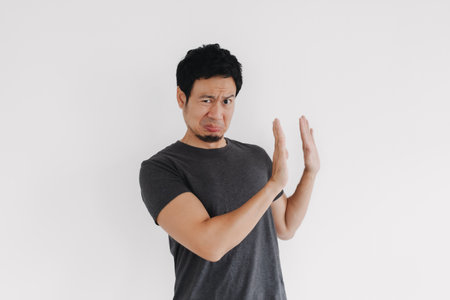 Thai male with hand raised signaling rejection in front of white wallの写真素材