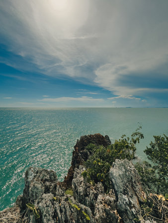 Tall cliff facing calm blue sea under vast cloudy sky in tropical locationの写真素材