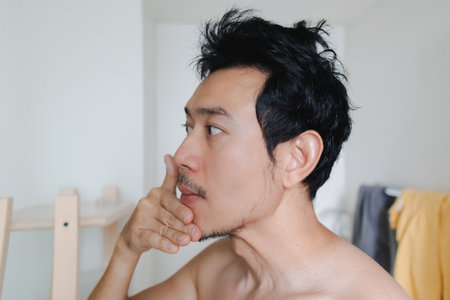 Thai male with focused look doing skincare in natural light at homeの写真素材