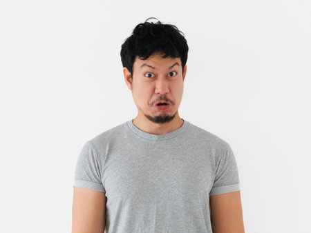 Facial expression of a startled Thai adult male with short hair and mustache standing against white...
